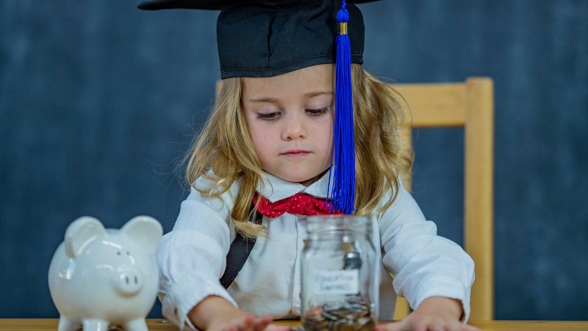 little girl with graduation cap and piggy bank counting money